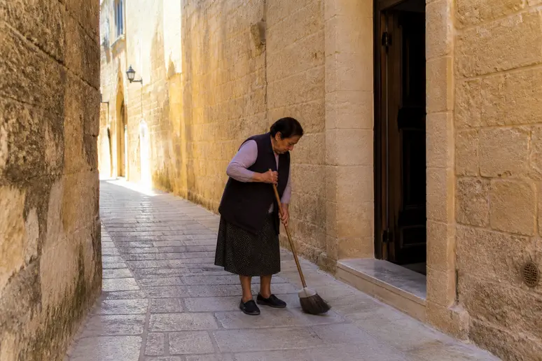 Une femme balaye une ruelle pavée à Mdina Malte, reflet de la vie paisible de la cité.