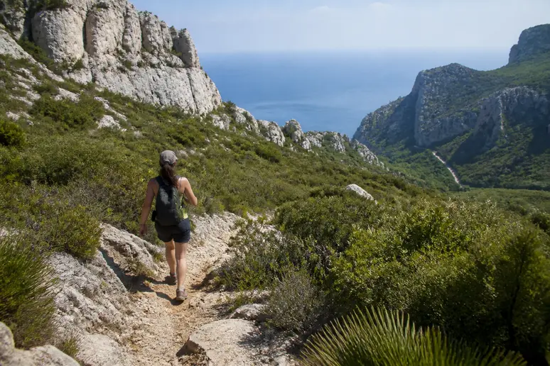 Randonneur marchant sur un sentier rocailleux escarpé lors de la descente vers la calanque de sugiton