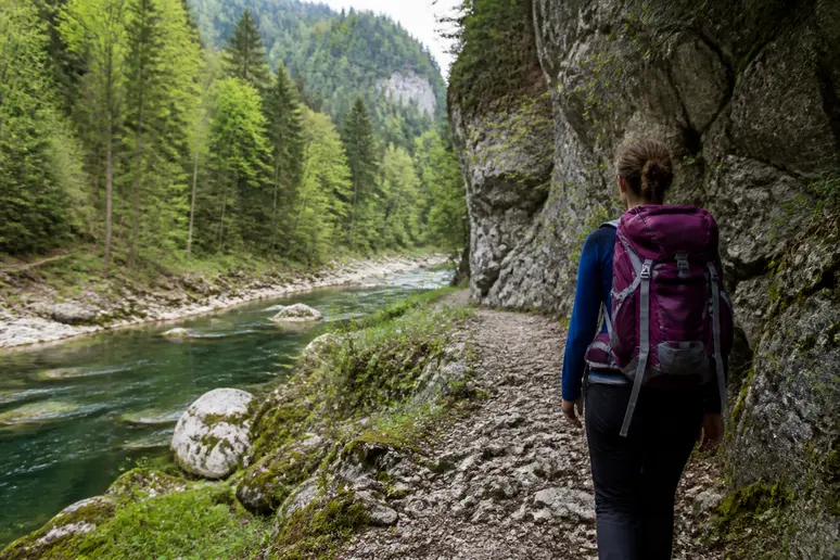 Randonneur marchant sur un sentier forestier rocailleux le long d'une rivière jurassienne