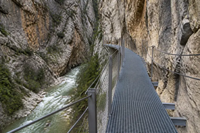 Passerelle suspendue en métal fixée le long des parois rocheuses au-dessus d'un torrent encaissé