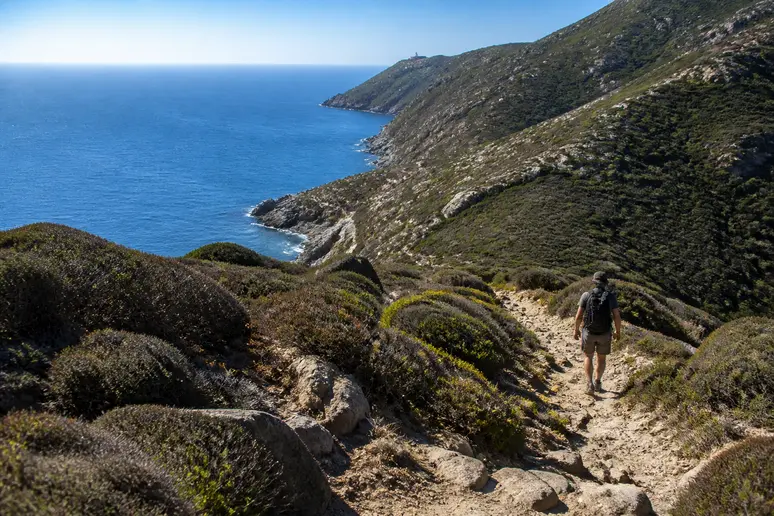 Randonneur marchant sur le sentier des douaniers caillouteux menant vers la plage de Barcaggio dans le Cap Corse
