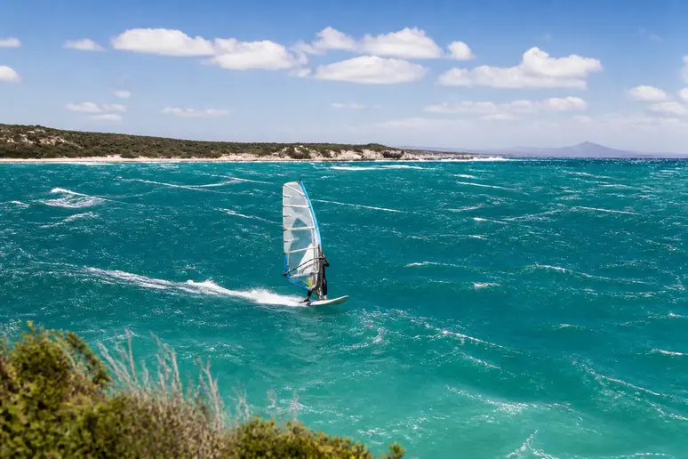 Planche à voile naviguant sur les eaux agitées du spot de kitesurf par vent d'ouest.