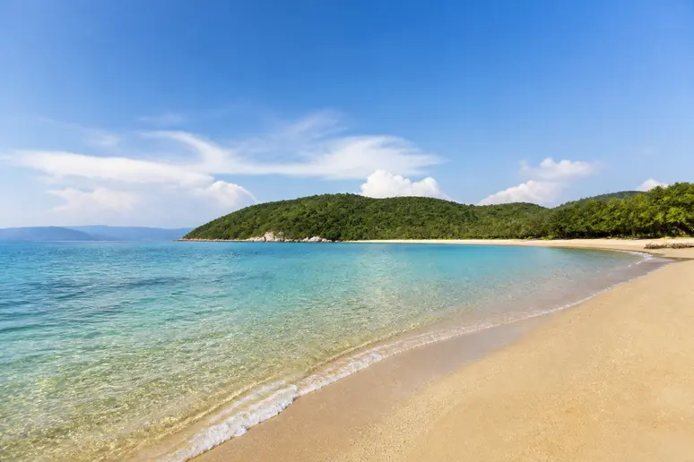 Eaux peu profondes et sable fin de la plage de Tamarone bordée de végétation.